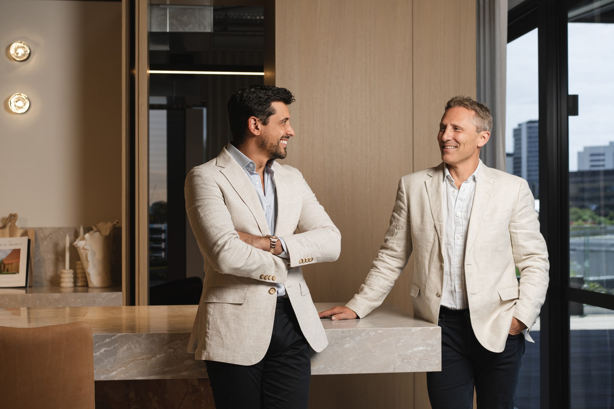 Two founders in linen blazers at a marble counter, smiling. Spyre Group