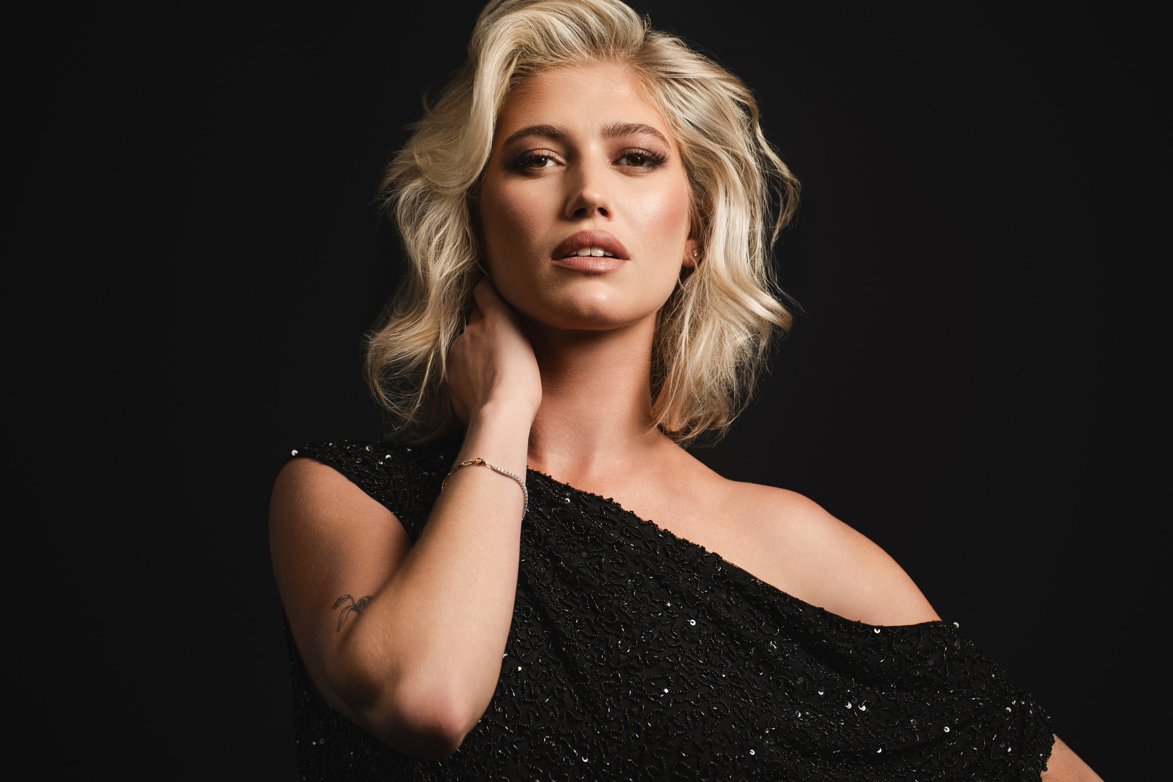 Blow Salon editorial portrait. Platinum-blonde model in a black sequinned off-shoulder dress against a black backdrop.