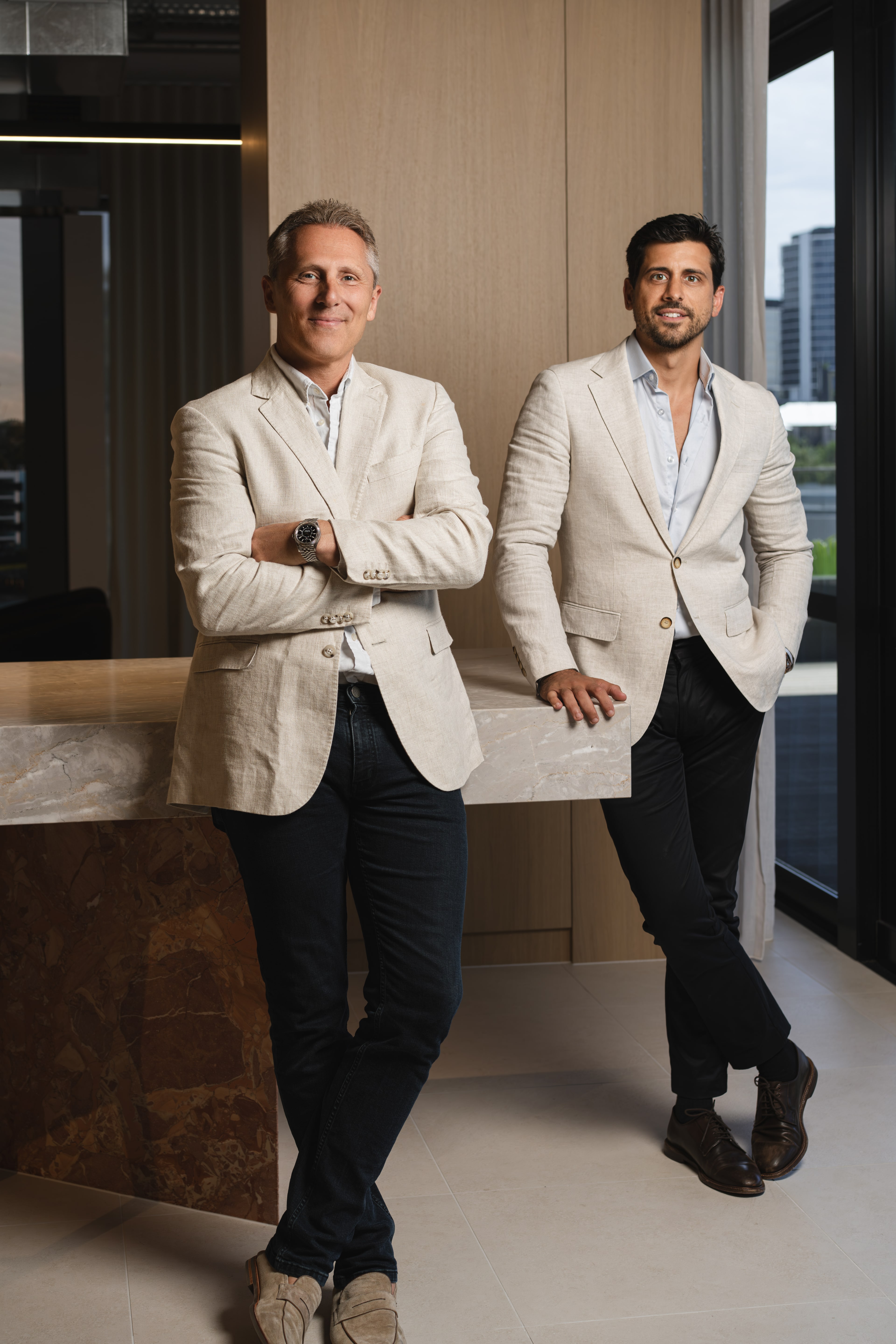 Spyre Group founders in linen blazers, leaning against a marble counter with city windows behind.